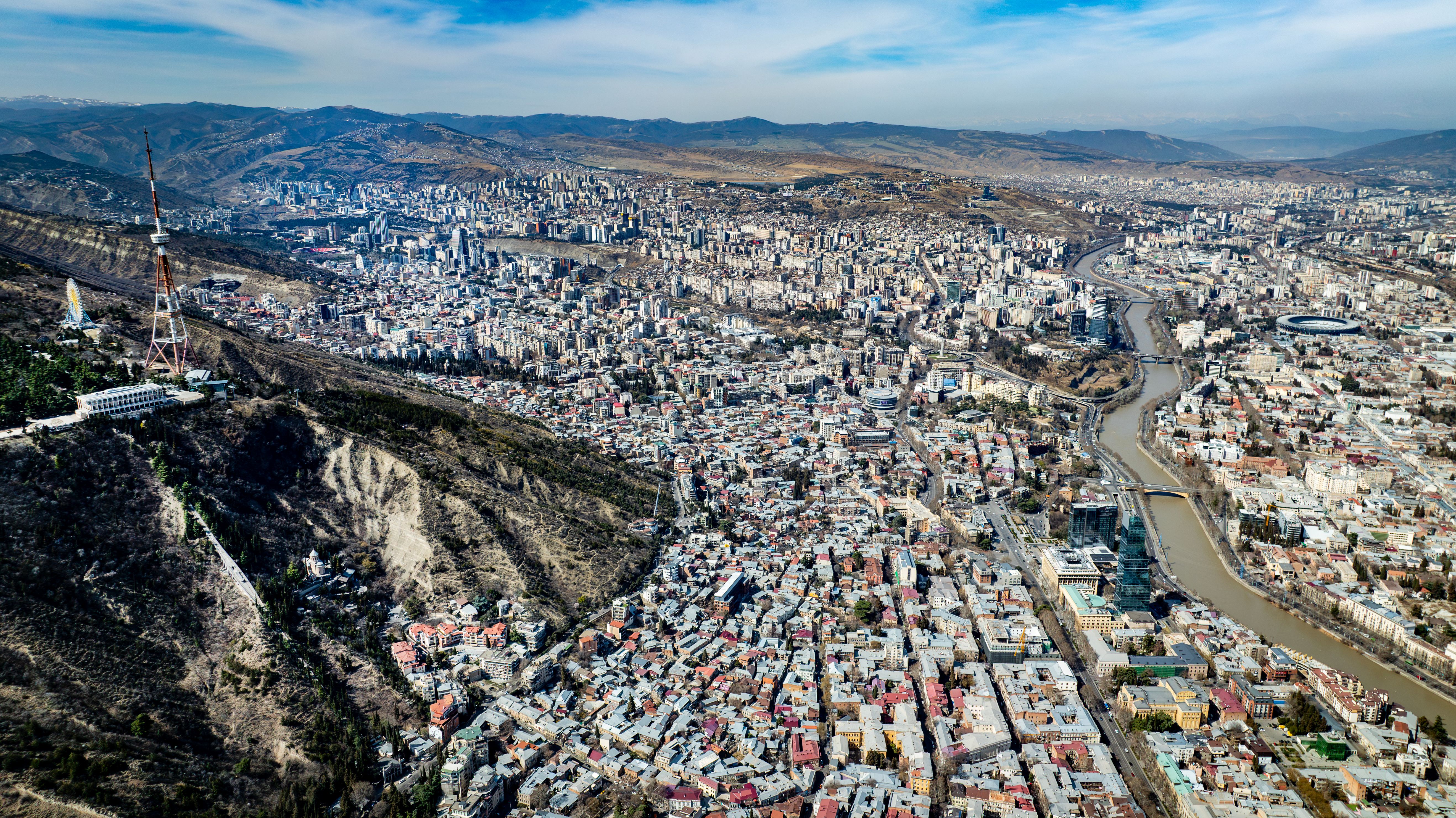 Aerial panoramic view of Tbilisi with the Mtkvari River, modern city and Caucasus mountain context